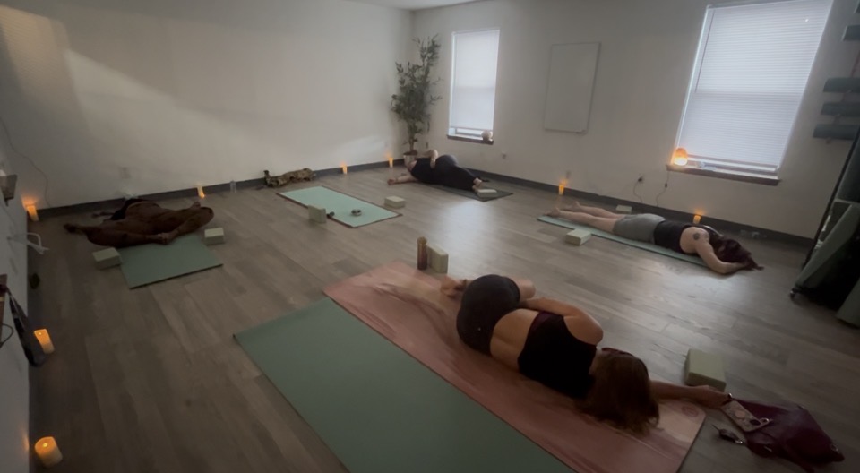 Students resting in a restorative pose on mats in the candlelit studio